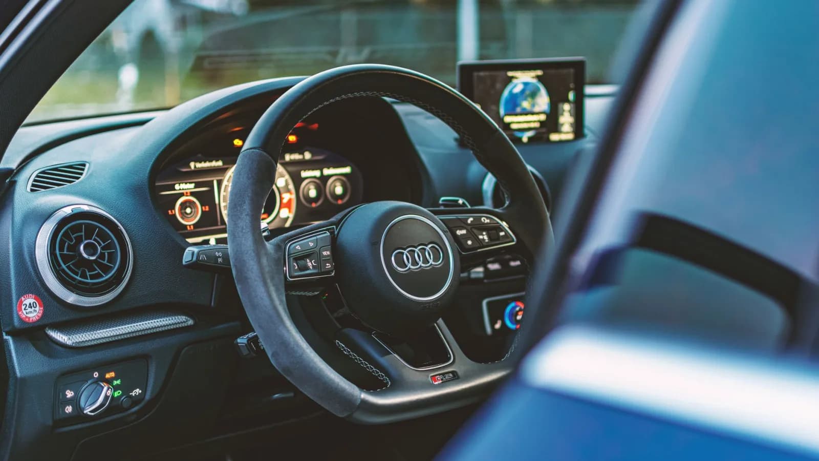 Pamje e brendshme e një automjeti Audi me fokus te timoni dhe pulti me kontrolle.